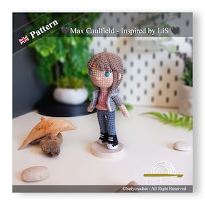 May include: Crocheted doll of Max Caulfield, inspired by Life is Strange. The doll has brown hair, blue eyes, and is wearing a gray jacket, pink shirt, and blue jeans. It stands on a wooden base. The image includes text that says "Pattern" and "Max Caulfield - Inspired by LiS".