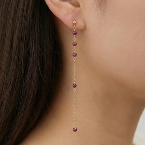 May include: A long, dangling earring featuring a thin gold chain adorned with five small, round, faceted deep pinkish-red gemstone beads spaced evenly along the length, finished with a gold stud post at the top of the earlobe.