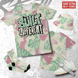 Könnte beinhalten: Eine Bekleidungskollektion mit einem Tarnmuster in Creme, Rosa und Grün. Enthält ein T-Shirt mit dem Text "BUILT DIFFERENT", einen Fischerhut, Socken und Sneaker. Die Artikel werden auf einer strukturierten, hellgrauen Oberfläche präsentiert.