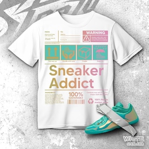 May include: White t-shirt with the text "Sneaker Addict" in a gradient color scheme. The shirt also features shipping label graphics and the words "100% Sustainable." A teal and gold sneaker is placed next to the shirt.