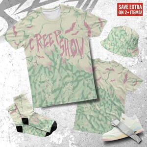 Könnte beinhalten: Eine Bekleidungskollektion mit dem Thema "Creep Show". Enthält ein T-Shirt, einen Fischerhut, Socken und Sneaker. Die Artikel weisen ein hellgrünes und rosa Tarnmuster mit Fledermäusen und Skeletten auf. Das T-Shirt hat die Worte "Creep Show" in Rosa.