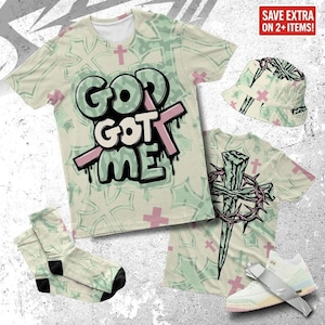 Könnte beinhalten: Eine Kollektion von Kleidung und Accessoires mit religiösem Thema. Enthält ein T-Shirt, einen Fischerhut, Socken und Turnschuhe. Das T-Shirt zeigt den Text "GOD GOT ME" im Graffiti-Stil. Die Artikel haben ein hellgrünes und rosa Farbschema.