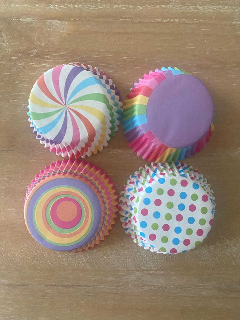 May include: Four colorful cupcake liners with different patterns. The liners are pink, purple, blue, green, orange, and yellow. The patterns include a swirl, polka dots, and concentric circles.