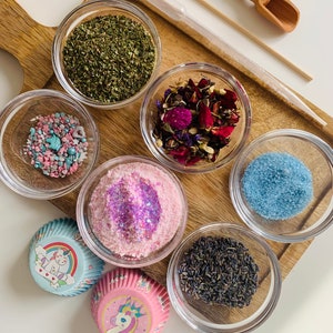 May include: A set of six small glass bowls filled with various ingredients, including dried herbs, flower petals, sprinkles, sugar, and lavender. Two unicorn-themed cupcake liners are also included.