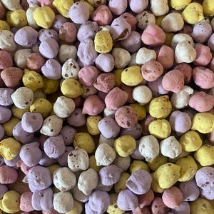 Pu&ograve; includere: Primo piano di una collezione di caramelle rotonde e colorate. Le caramelle sono in vari colori pastello, tra cui giallo, rosa, viola e bianco. Alcune caramelle hanno motivi maculati. Le caramelle sembrano essere un tipo di confetteria.