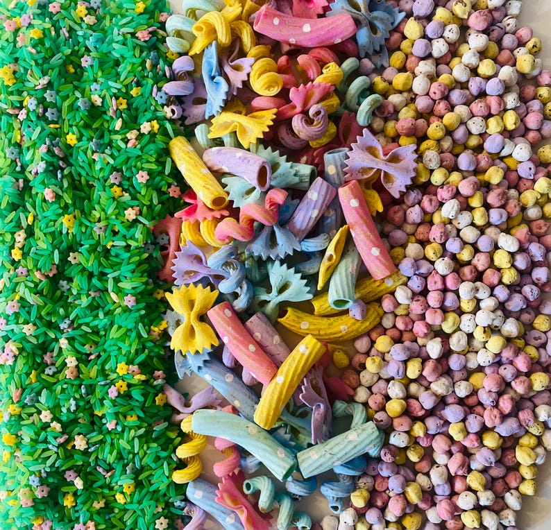 Pu&ograve; includere: Una vista dall'alto mostra un assortimento colorato di pasta e riso tinti. L'immagine &egrave; divisa in tre sezioni verticali: riso verde con minuscoli fiori, un mix di forme di pasta dai colori pastello e piccole perle rotonde e macchiate.