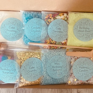 May include: A set of ten clear plastic bags filled with various cake decorating supplies. The bags are labeled with the following: Cake Frosting, Confetti Crystals, Cake Sprinkles, Birthday Wish Dust, Birthday Gift Surprises, Cake Crumbs, Mini Birthday Balloons, Melting Candles.