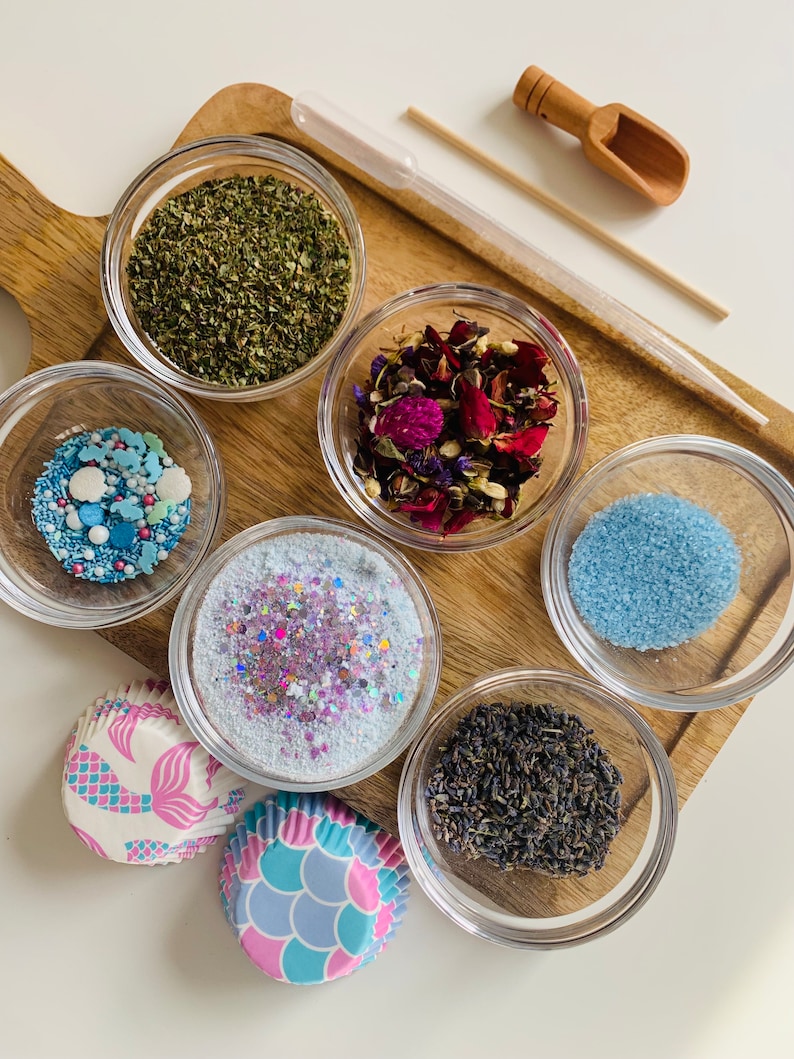 May include: Six small glass bowls filled with various ingredients, including dried herbs, flower petals, glitter, and sprinkles. Two mermaid-themed cupcake liners are also included.