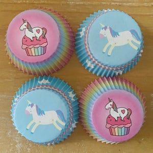 May include: Four cupcake liners with unicorn designs. Two liners feature a unicorn on a cupcake, set against a pink background. The other two have a unicorn on a blue background. The liners have a rainbow-colored, ruffled edge.