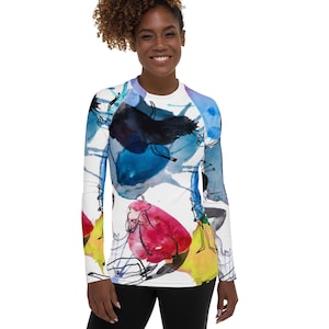 May include: A white long-sleeve shirt with a colorful abstract design featuring blue, yellow, red, and black watercolor-like shapes. The design includes abstract figures and lines.