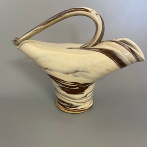 May include: A white ceramic pitcher with a brown swirl design and a unique curved handle.