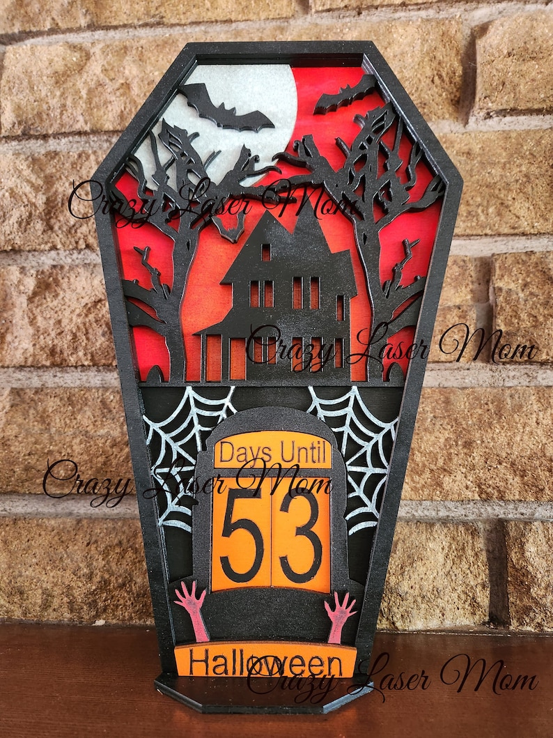 May include: Black wooden Halloween countdown sign shaped like a coffin with a haunted house, bats, and a full moon. The sign says "Days Until Halloween" and shows the number "53".