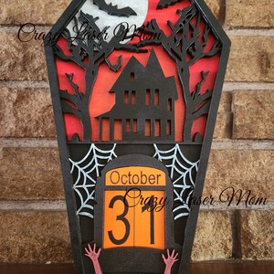 May include: Black wooden coffin-shaped Halloween countdown calendar with a haunted house, bats, and a full moon. The calendar features a spooky spiderweb and the date October 31st.
