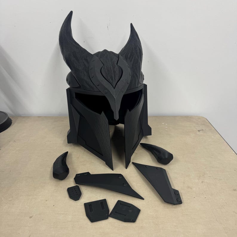 Puede incluir: Un casco de pl&aacute;stico negro con cuernos y una superficie texturizada. El casco est&aacute; desmontado en varias piezas, incluyendo los cuernos, la parte superior del casco y la visera.