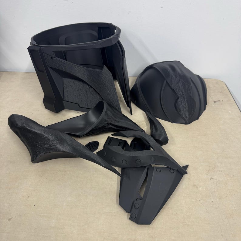 Puede incluir: Un conjunto de piezas de pl&aacute;stico negro para un disfraz, posiblemente un casco o una armadura. Las piezas son texturizadas y tienen un aspecto &aacute;spero y sin terminar.