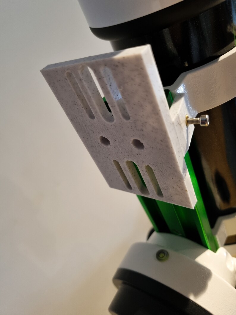 Pu&ograve; includere: Una staffa bianca stampata in 3D con tre fessure e due fori, fissata a un supporto per telescopio verde e bianco.