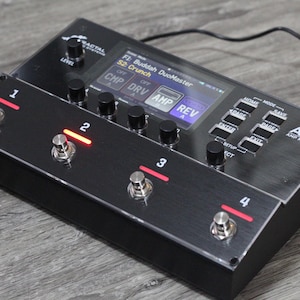 May include: Black AM4 amp modeler with four footswitches and a digital display. The display shows "F1: Buddah DuoMaster" and "S2: Crunch". The device has several knobs and buttons for adjusting settings. The footswitches have red indicator lights.