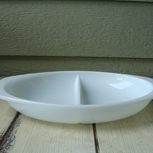 May include: White oval divided serving dish with two sections. The dish is made of ceramic and has a smooth, glossy finish.