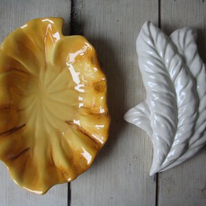 May include: Two ceramic dishes in the shape of leaves. One dish is yellow and the other is white.
