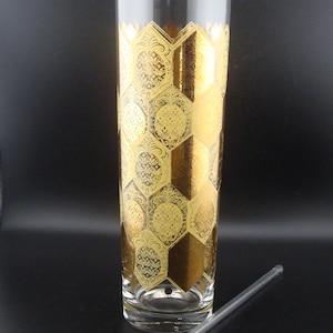 May include: A tall, clear glass vase with a gold honeycomb pattern and a clear glass stirring rod. The vase has a flared top with two small spouts. The gold pattern is ornate and covers most of the vase.