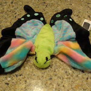 May include: A green and black butterfly plush toy with rainbow wings and a Ty tag. The tag is red with white text that says "Beanie Babies".