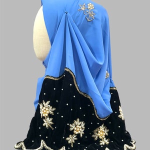 Puede incluir: Un hiyab azul claro con ribete de terciopelo negro y adornos florales de perlas y oro.