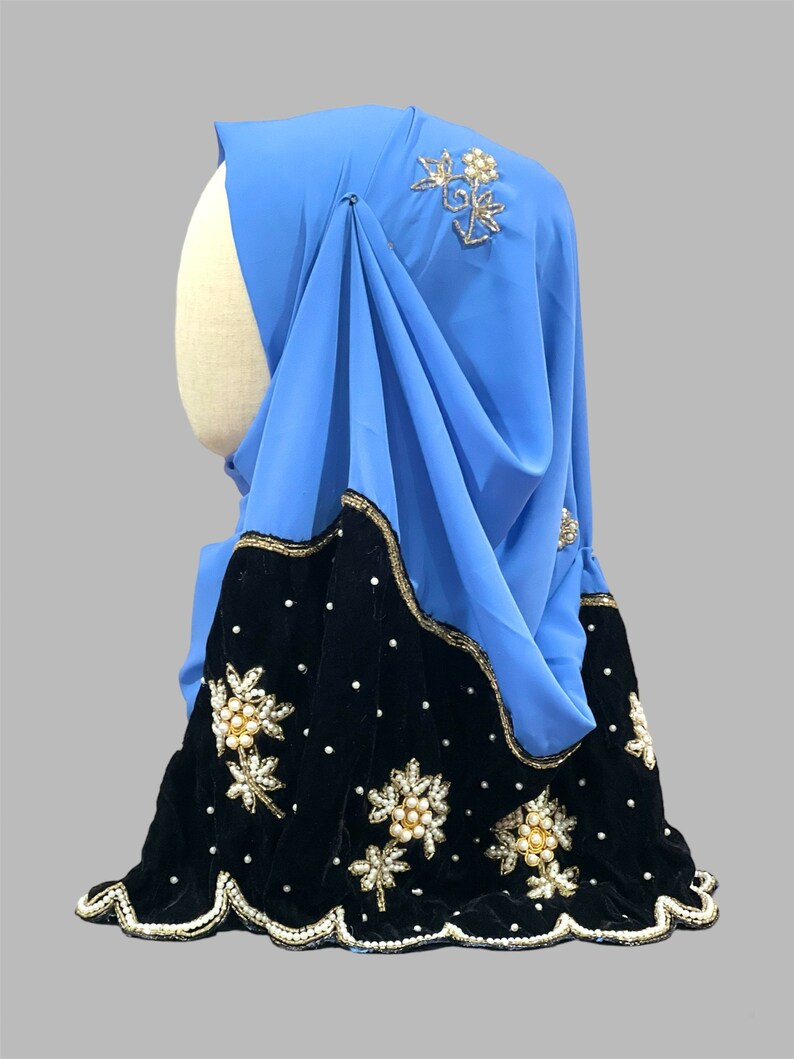 Puede incluir: Un hiyab azul claro con ribete de terciopelo negro y adornos florales de perlas y oro.