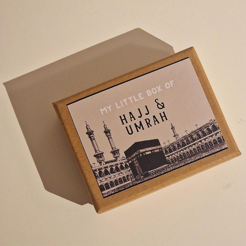 May include: A brown box with a white label that says "My Little Box of Hajj & Umrah". The label features a black and white illustration of the Kaaba and the surrounding buildings in Mecca.