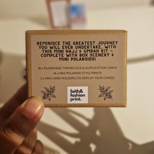 May include: A brown box with the text "REMINISCE THE GREATEST JOURNEY YOU WILL EVER UNDERTAKE, WITH THIS MINI HAJJ & UMRAH KIT - COMPLETE WITH BOX SCENERY & MINI POLAROIDSI" and "faith&fashion print."  The box contains 18 pilgrimage-themed dua & supplication cards, 14 mini polaroid style prints, and 2 mini card holders.