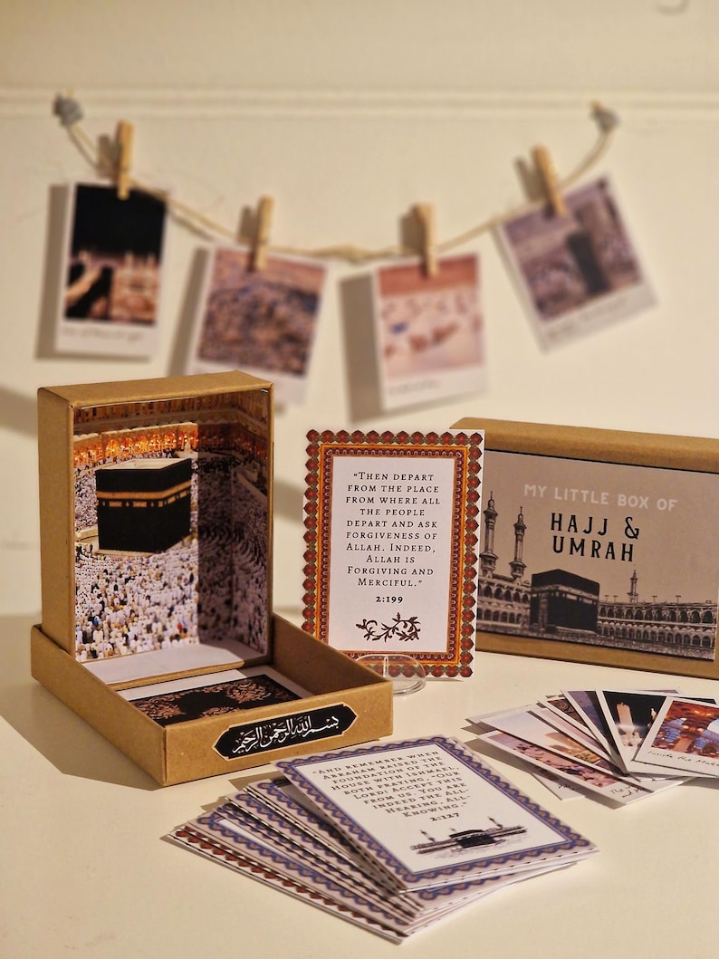 May include: A small box with a brown exterior and a picture of the Kaaba on the front. The box contains a set of cards with Islamic quotes and images related to Hajj and Umrah. The box is labeled "My Little Box of Hajj & Umrah".