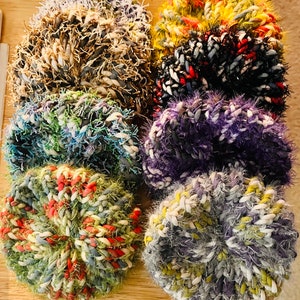 May include: Six colorful crocheted scrubbies in various colors, including purple, blue, green, red, white, and yellow.
