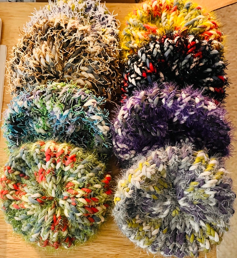 May include: Six colorful crocheted scrubbies in various colors, including purple, blue, green, red, white, and yellow.