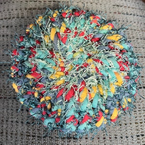 May include: A round, multi-colored braided rug with a fuzzy texture. The rug is made with red, yellow, blue, and green yarn.
