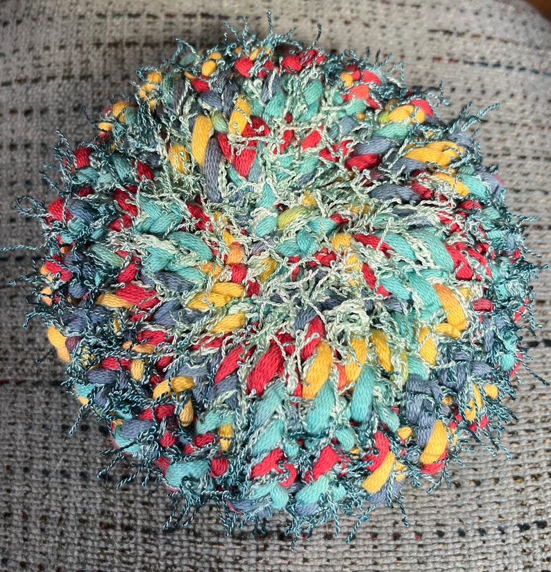 May include: A round, multi-colored braided rug with a fuzzy texture. The rug is made with red, yellow, blue, and green yarn.