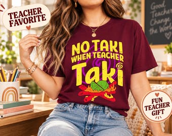 Op de afbeelding: Een bordeauxrood t-shirt met korte mouwen en de gele tekst NO TAKI WHEN TEACHER Taki, een paarse spiraalafbeelding en een groen limoenpartje op rode en gele gestileerde vlammen op de voorzijde van het kledingstuk.