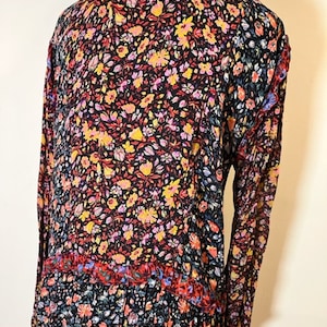 May include: A long-sleeved dress with a high neck and a floral print in shades of red, yellow, pink, and blue on a black background. The dress has a tiered skirt and a ruffled neckline.