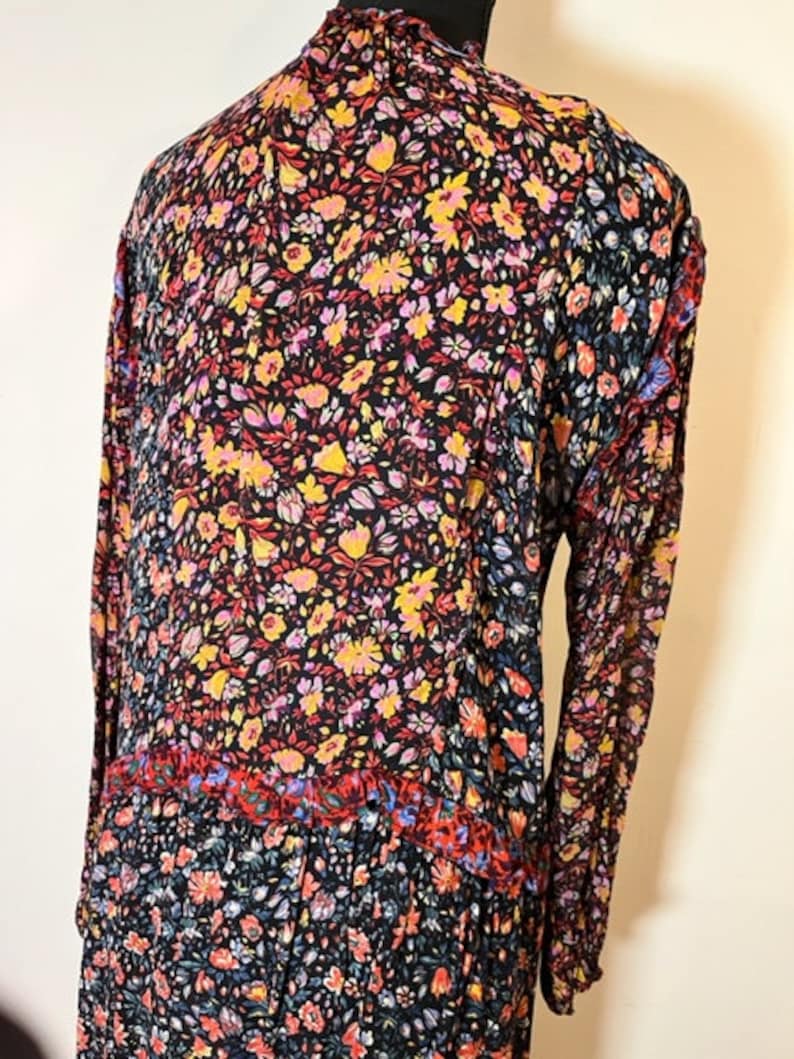 May include: A long-sleeved dress with a high neck and a floral print in shades of red, yellow, pink, and blue on a black background. The dress has a tiered skirt and a ruffled neckline.
