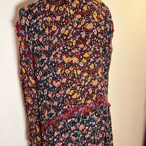 May include: A long-sleeved dress with a floral print in shades of red, yellow, blue, and black. The dress has a ruffled neckline and a tiered skirt.