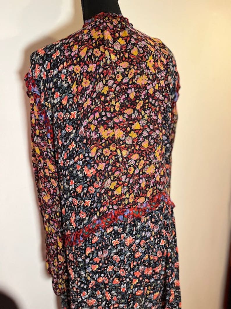 May include: A long-sleeved dress with a floral print in shades of red, yellow, blue, and black. The dress has a ruffled neckline and a tiered skirt.