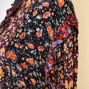 May include: A black long-sleeved blouse with a floral print in shades of red, pink, yellow, and blue. The blouse has a ruffled collar and cuffs.