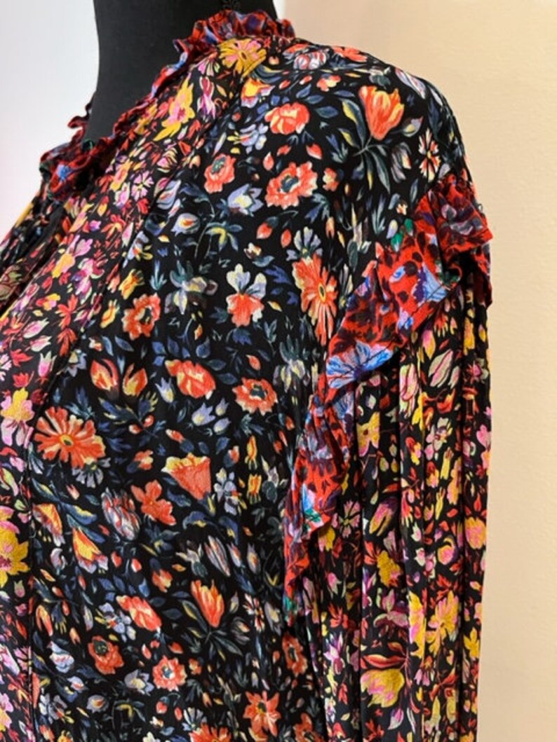 May include: A black long-sleeved blouse with a floral print in shades of red, pink, yellow, and blue. The blouse has a ruffled collar and cuffs.
