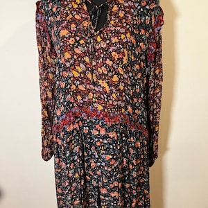 May include: A long-sleeved floral dress with a tie at the neck. The dress has a black background with a multi-coloured floral pattern. The dress has a tiered skirt.