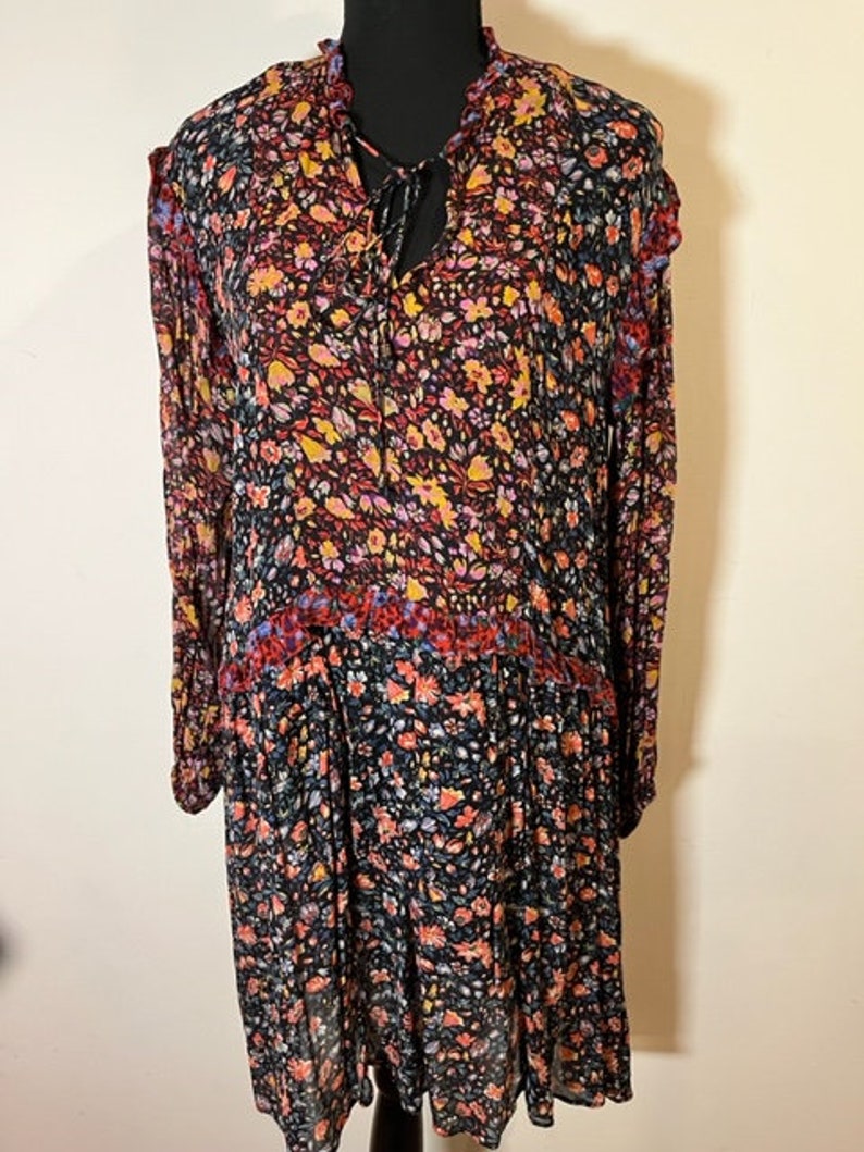 May include: A long-sleeved floral dress with a tie at the neck. The dress has a black background with a multi-coloured floral pattern. The dress has a tiered skirt.