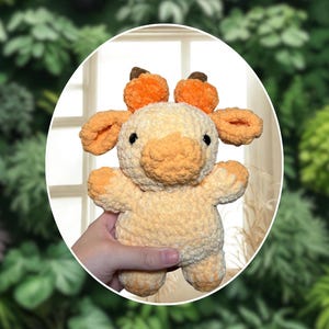 Può includere: Un peluche a forma di giraffa realizzato a mano all'uncinetto, nei toni del crema e dell'arancione. La giraffa ha piccole corna, orecchie e muso arancioni. Il peluche è morbido e coccoloso, perfetto come giocattolo per bambini o per l'arredamento della cameretta.