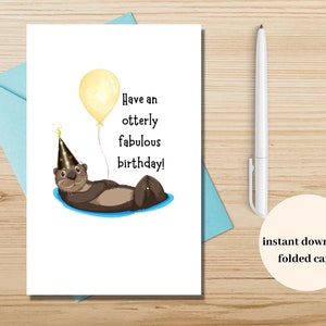 Könnte beinhalten: Eine gefaltete Geburtstagskarte mit einer Illustration eines Otters mit Partyhut und gelbem Ballon. Auf der Karte steht "Have an otterly fabulous birthday!". Ein weißer Stift und ein blauer Umschlag sind ebenfalls zu sehen.