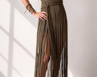 Pode incluir: Um vestido de macramé verde-oliva com decote halter, detalhes intrincados de nós no corpete e uma saia longa com franjas que vai até ao chão. A peça inclui uma faixa de cintura a condizer e uma pulseira coordenada em macramé.