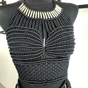 Black luxurious macramé top with metallic details, worn by a model, perfect for festivals, parties, or the beach, showcasing intricate handmade craftsmanship and a stylish, bold design.
