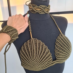 May include: A green macrame bikini top with a shell-shaped design. The top is made with a thick cord and has adjustable straps. The top is displayed on a black mannequin.