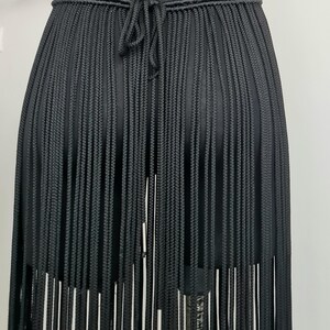 Close-up of the back view of a black macramé skirt, showcasing intricate patterns and detailed craftsmanship, with a focus on the ties and design.