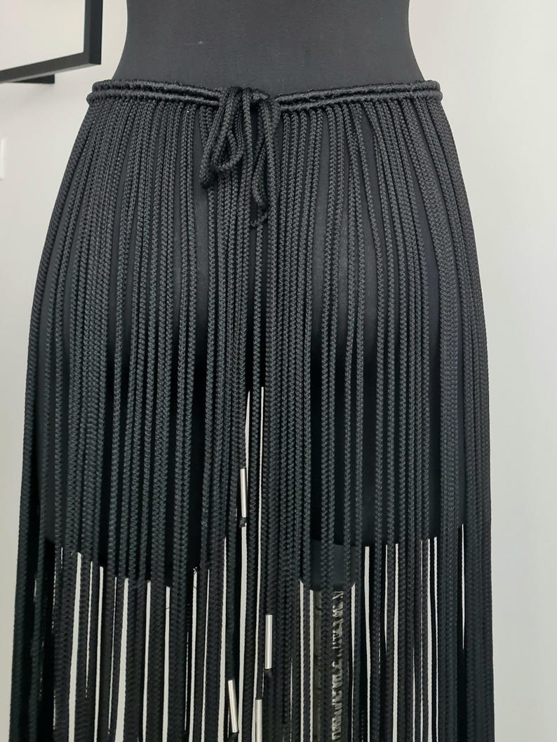 Close-up of the back view of a black macramé skirt, showcasing intricate patterns and detailed craftsmanship, with a focus on the ties and design.